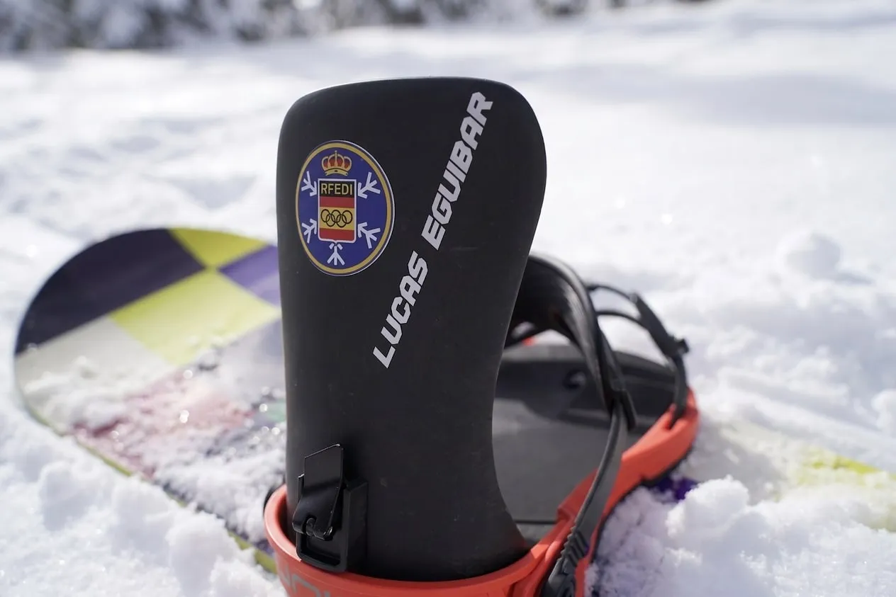 Made-to-measure carbon piece with the Spain Snow crest mounted on a snowboard binding in the snow